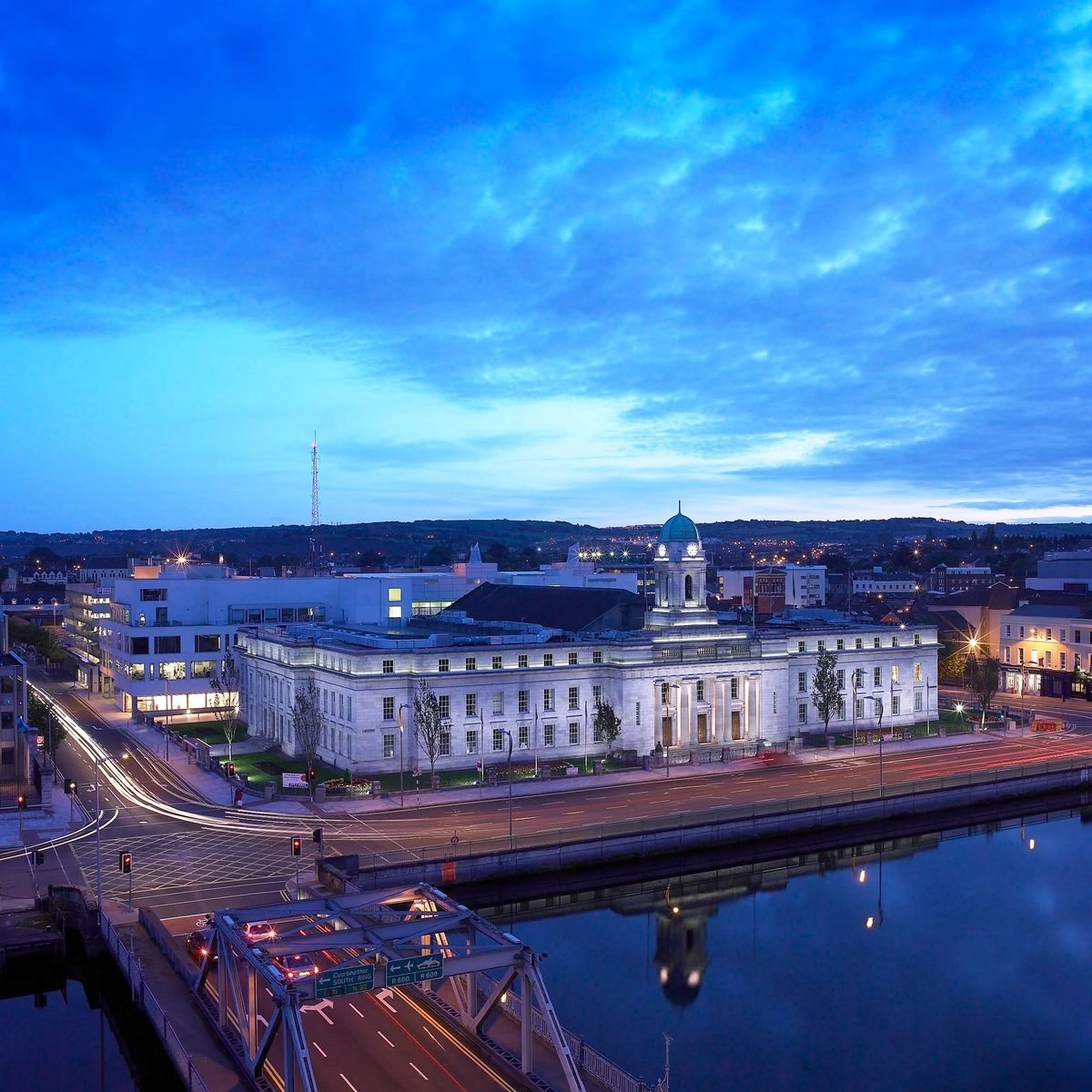 Cork City Hall illuminated at dusk beside the River Lee